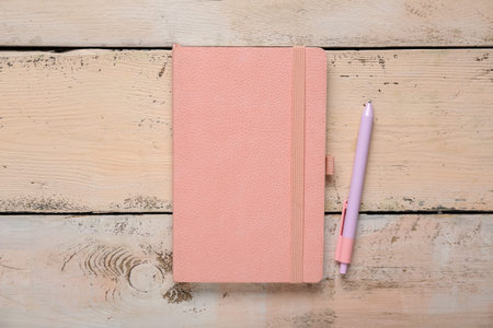 Composition with pink notebook and pen on beige wooden background, closeup