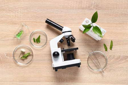 Modern microscope with different leaves and petri dishes on wooden background