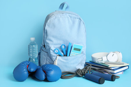 Backpack, school supplies and sports equipment on blue background