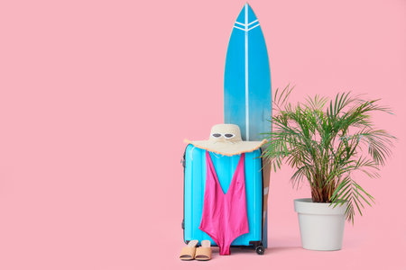 Suitcase with beach accessories, surfboard and palm tree on pink backgroundの写真素材