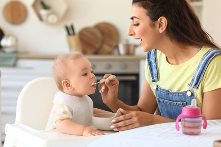 Young mother feeding her baby in high chair at homeの写真素材