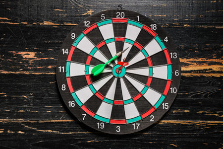 Board with darts on wooden background