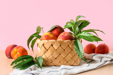 Wicker basket of fresh peaches on pink backgroundの写真素材