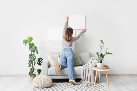 Young woman hanging painting on white wall in living roomの写真素材
