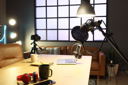 Podcaster's workplace with laptop, microphone and glowing lamps in dark studio