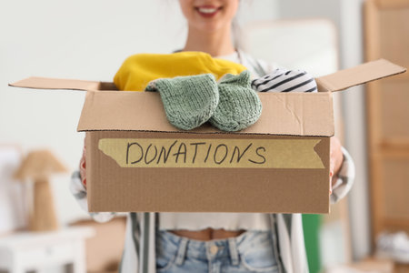 Young woman holding box with clothes for donation in bedroom, closeup