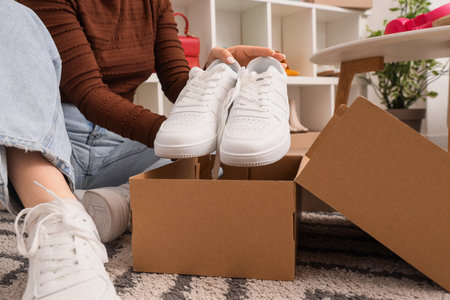 Woman putting white sneakers into shoe box at home, closeupの写真素材