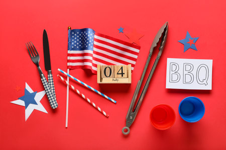 USA flag, card with letters BBQ, calendar with date 04 JULY and barbecue utensils on red background. Independence Day celebrationの写真素材