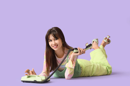 Stylish young woman with telephone lying on lilac background