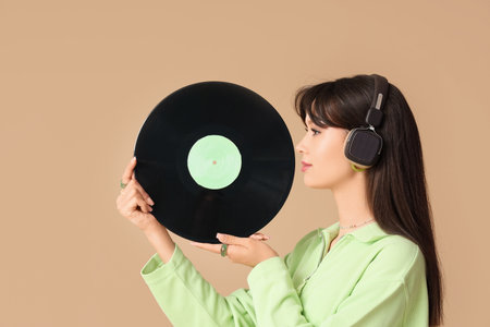 Stylish young woman in headphones with vinyl disk on beige backgroundの写真素材