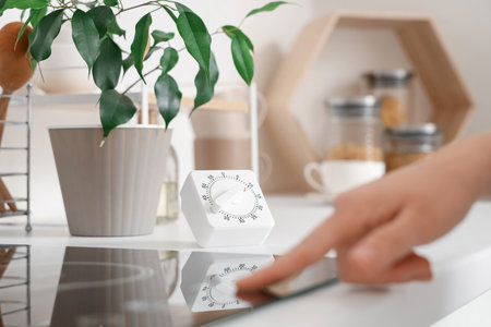 Kitchen timer and female hand turning on stove in room, closeupの写真素材