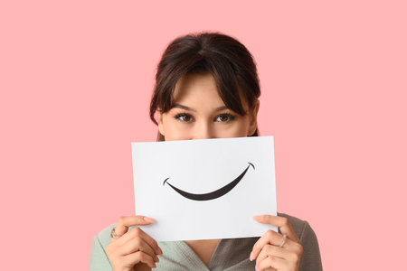 Young woman with paper smile on pink background, closeup