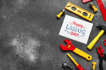 Toy construction tools and greeting card with text HAPPY LABOR DAY on gray grunge background. Labor...