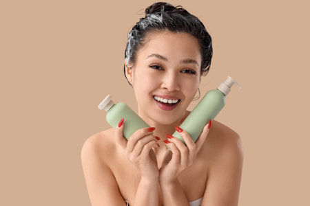 Pretty young Asian woman with bottles of shampoo on beige backgroundの写真素材