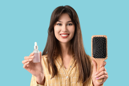 Young woman with serum for hair growth and brush on blue background
