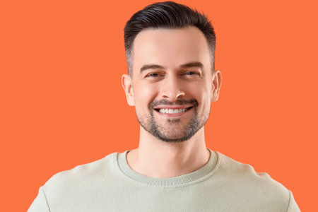 Young man with beautiful smile on orange background, closeup