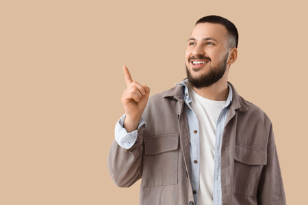 Young man with beautiful smile pointing at something on beige backgroundの写真素材