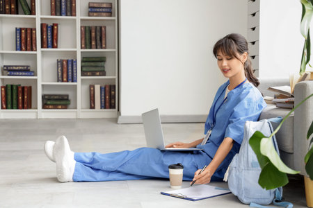 Female medical intern studying with laptop on floor in library