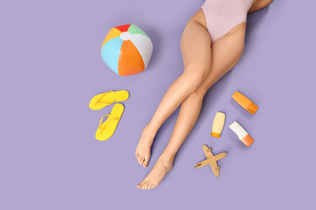 Young woman with beach accessories and wooden airplane on lilac background