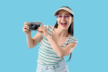 Stylish young woman in summer cap with photo camera on blue background