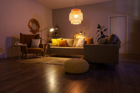 Interior of stylish living room with cozy gray sofas, armchair and glowing lamps at evening