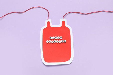 Paper blood pack for transfusion with text BLOOD DONATION on purple background. Blood donation...
