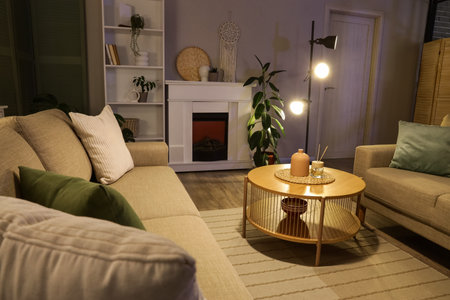 Interior of stylish living room with gray sofas, coffee table, fireplace and glowing lamps at eveningの写真素材