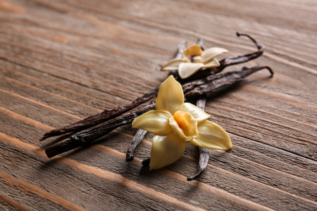 Vanilla sticks and flowers on wooden background, closeup