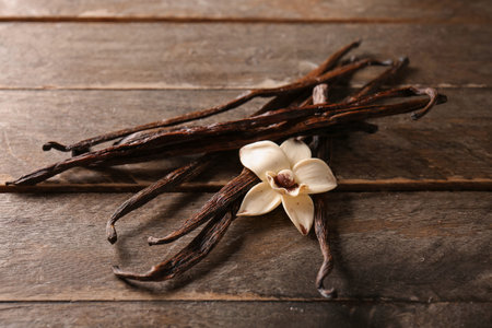 Vanilla sticks and flowers on wooden background