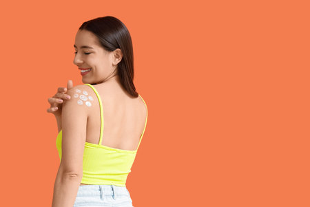 Young woman with sunscreen cream on orange background