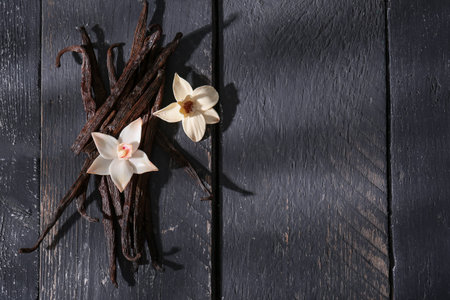Vanilla sticks and flowers on dark wooden background, top view