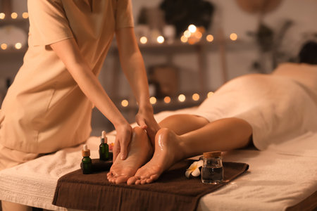 Female therapist massaging woman's foot on table in dark spa salonの写真素材