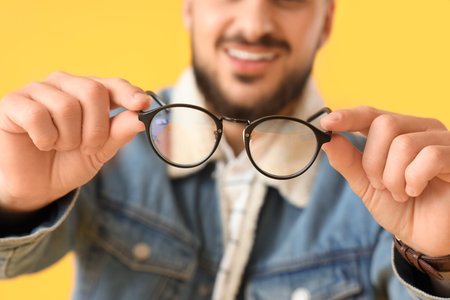 Handsome young man showing eyeglasses on yellow backgroundの写真素材