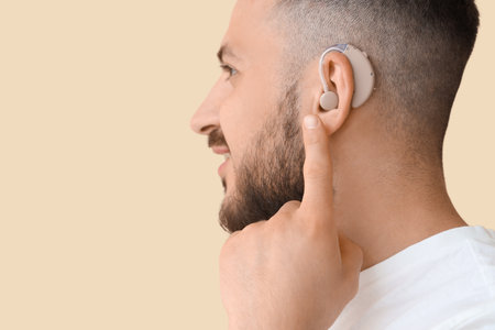 Young man with hearing aid on beige background, closeupの写真素材