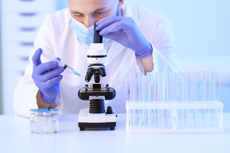 Male scientist with syringe and ampules looking through microscope in laboratory, closeupの写真素材