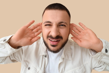 Young man with hearing problem on beige background, closeupの写真素材