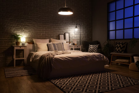 Interior of dark bedroom with tables, armchair and glowing lampsの写真素材