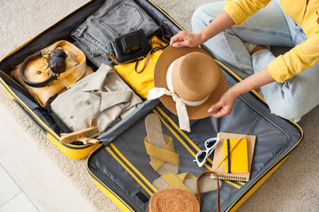 Young woman packing travel accessories into suitcase at home, top view