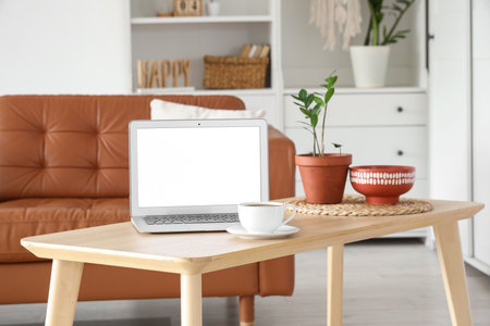 Modern laptop and cup of coffee on wooden coffee table in living room, closeupの写真素材