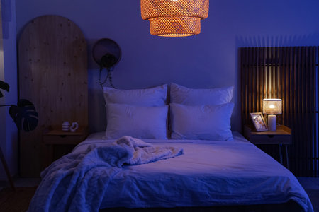 Interior of dark room with bed, tables and glowing lamps at nightの写真素材