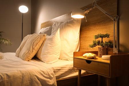 Glowing lamp with bonsai tree on table in dark bedroomの写真素材