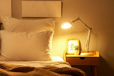 Glowing lamp with cactus and frame on table in bedroom at nightの写真素材