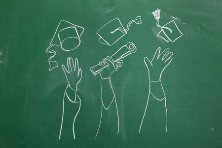 Drawn hands with diploma and graduation hats on green chalkboardの写真素材