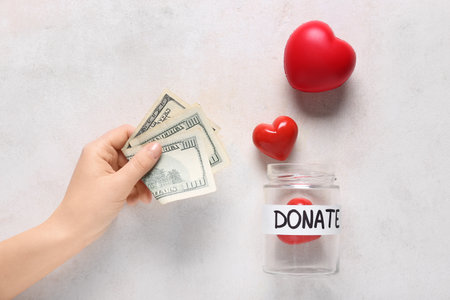 Jar with red hearts and hand with dollar banknotes on light grunge background. Donation conceptの写真素材