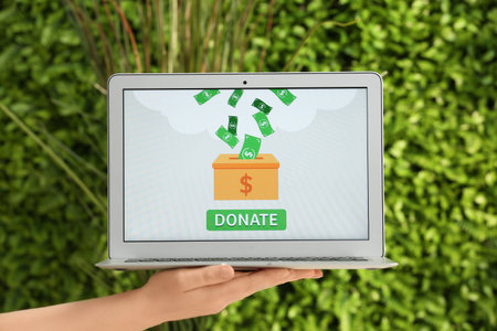 Hand holding laptop with open page of donation website outdoorsの写真素材