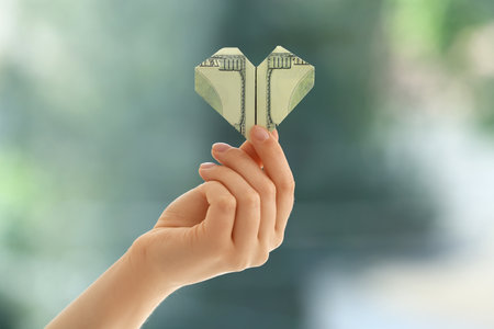 Hand holding dollar banknote in shape of heart on blurred background. Donation conceptの写真素材