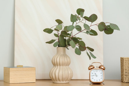 Vase with beautiful eucalyptus branches, clock and decor on table near white wall, closeupの写真素材