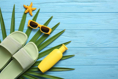 Composition with bottle of sunscreen cream and beach accessories on blue wooden background