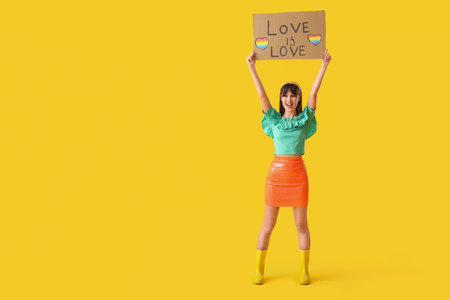 Beautiful young woman holding placard with text LOVE IS LOVE on yellow background. LGBT conceptの写真素材