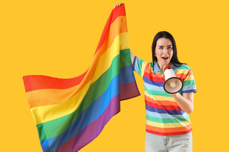 Beautiful young woman in rainbow t-shirt with LGBT flag and megaphone on yellow backgroundの写真素材